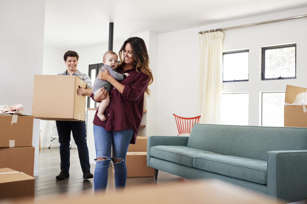 Family With Baby Carrying Boxes Into New Home On Moving Day