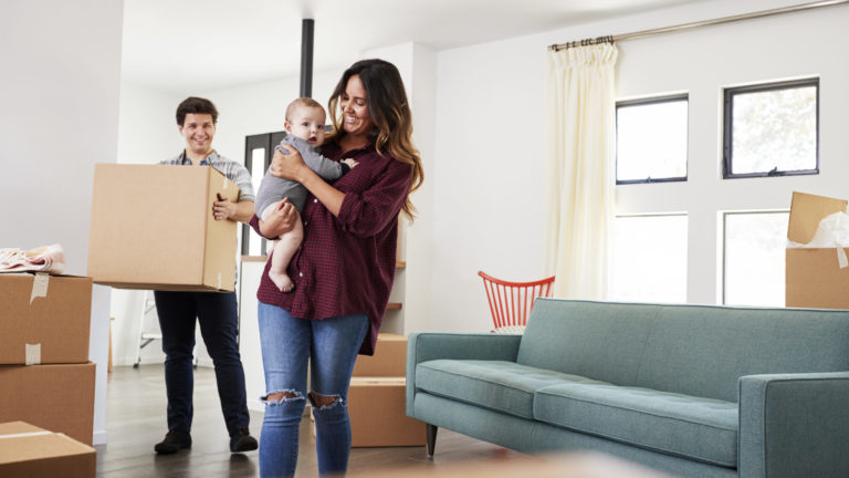 Family With Baby Carrying Boxes Into New Home On Moving Day