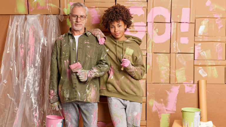 Indoor shot of mixed race senior man and adult woman hold paint brushes busy doing repair at home to